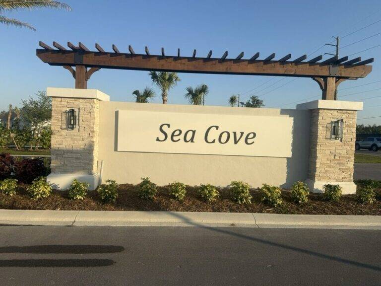 Brown pergola monument sign with stacked stone and wall lanterns Sea Cove Florida