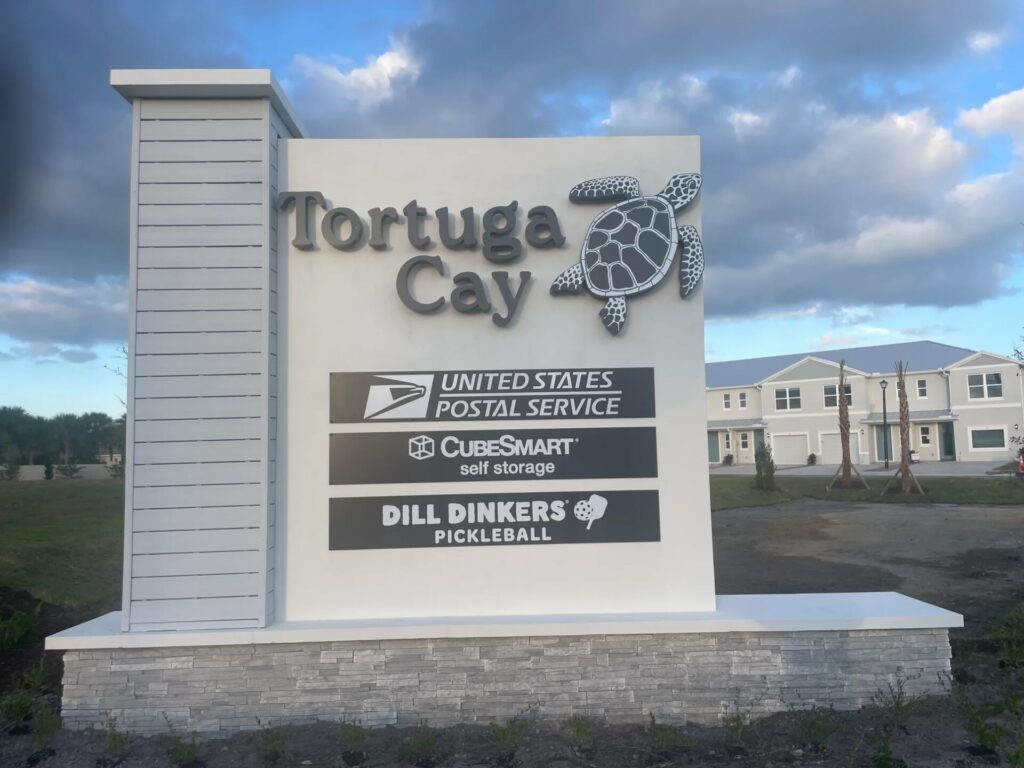 White precast monument sign with turtle logo for Tortuga Cay coastal community Florida